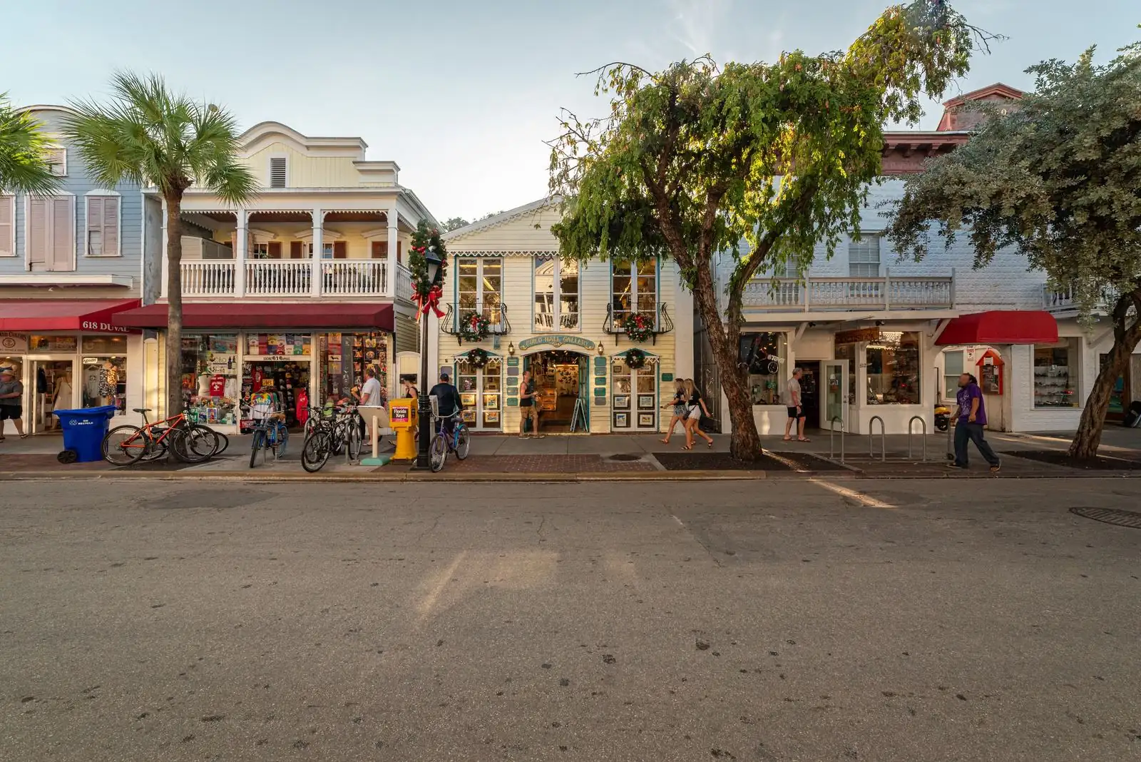 Palm-lined Naples street at dusk with lit outdoor cafe tables and brick sidewalks