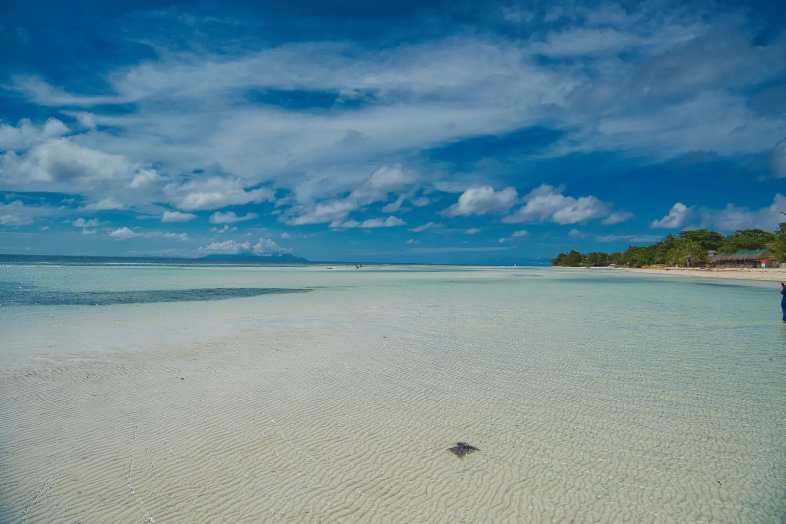 Undeveloped white sand island beach with clear shallow water and a boat anchored offshore