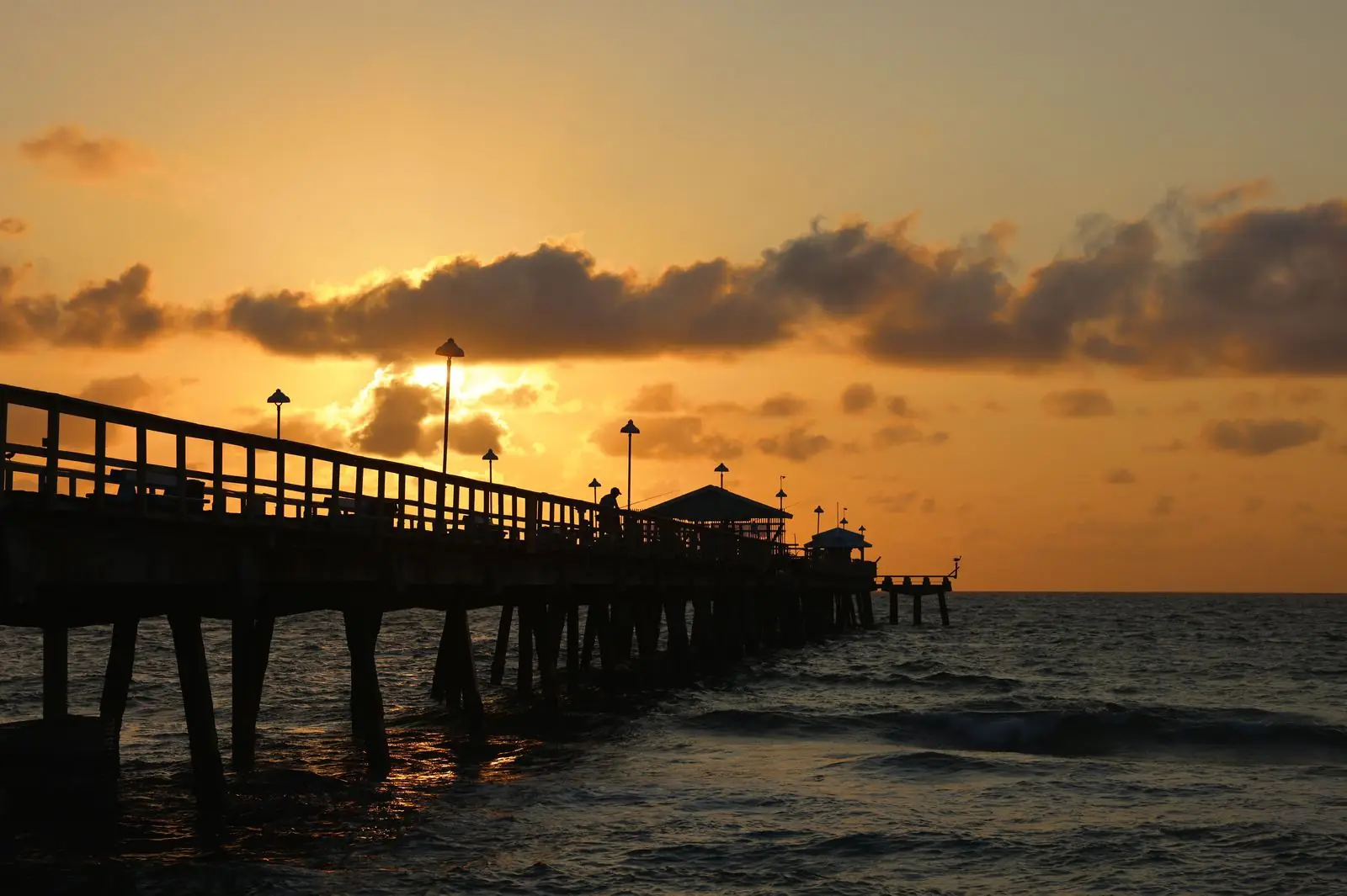 Naples Pier pilings and deck lit by warm golden hour light above calm Gulf water